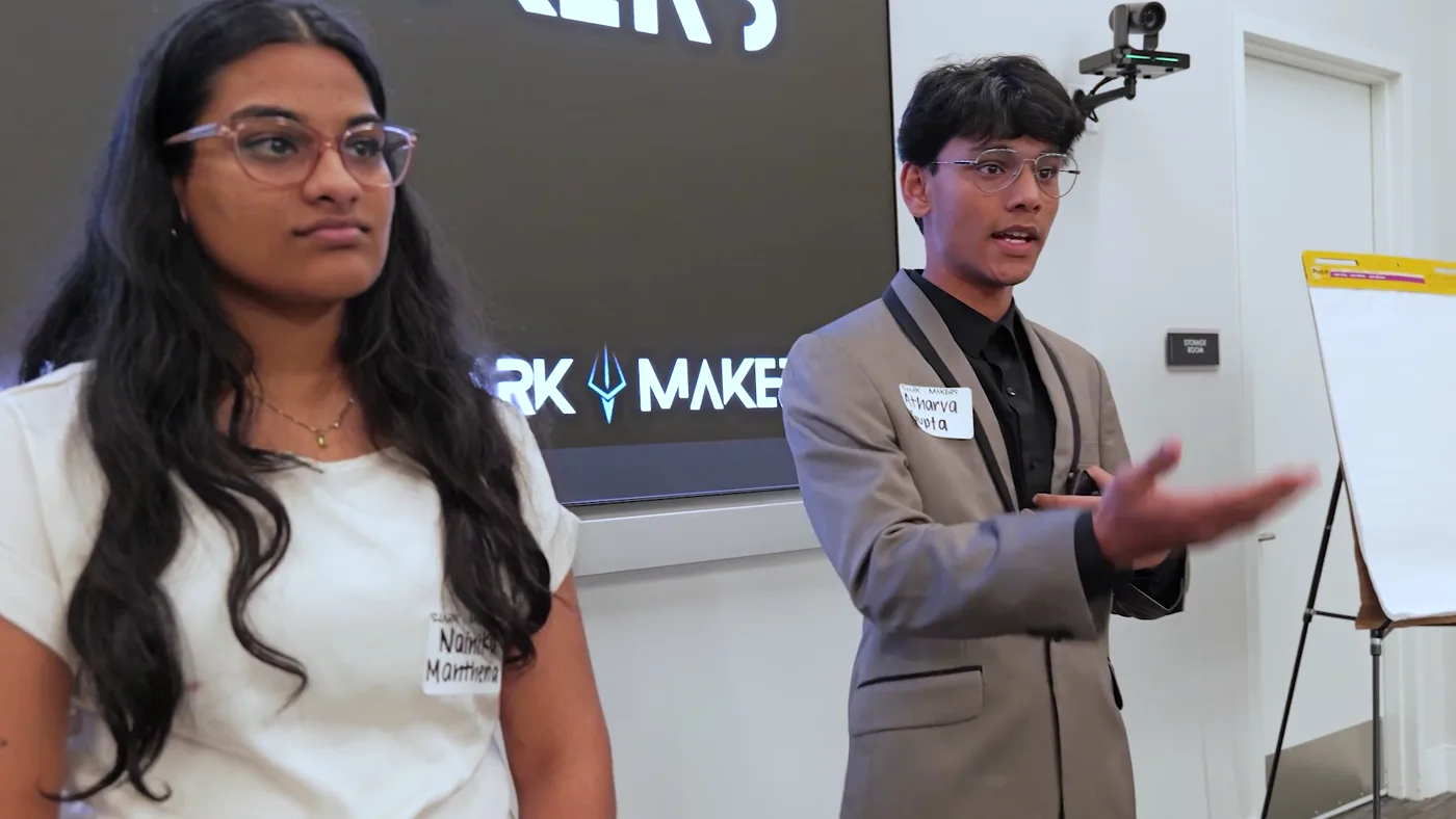 Two students presenting to the room in front of a SharkMakers backdrop.