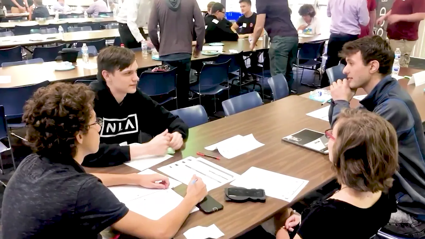 A SharkMakers workshop in progress, with students working in teams around tables while a mentor circulates.
